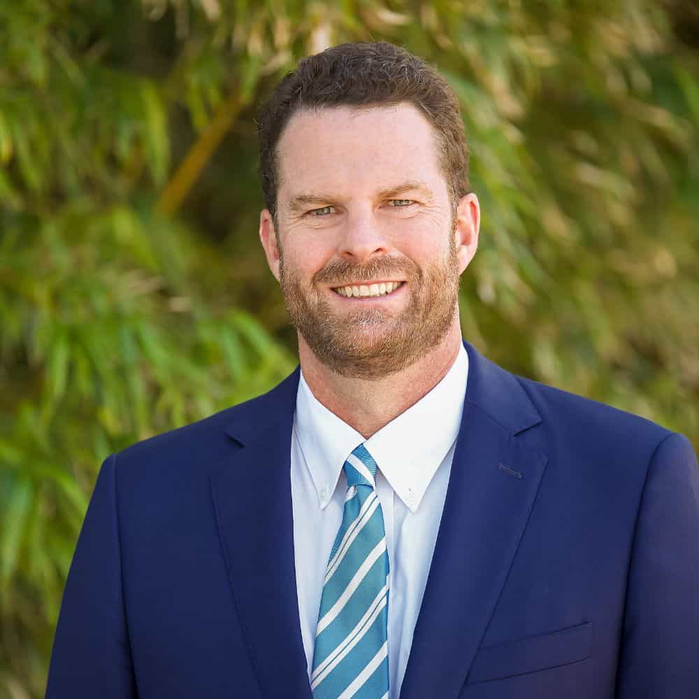 Smiling man in professional suit outdoors, representing leadership and confidence, ideal for business or political profile images.