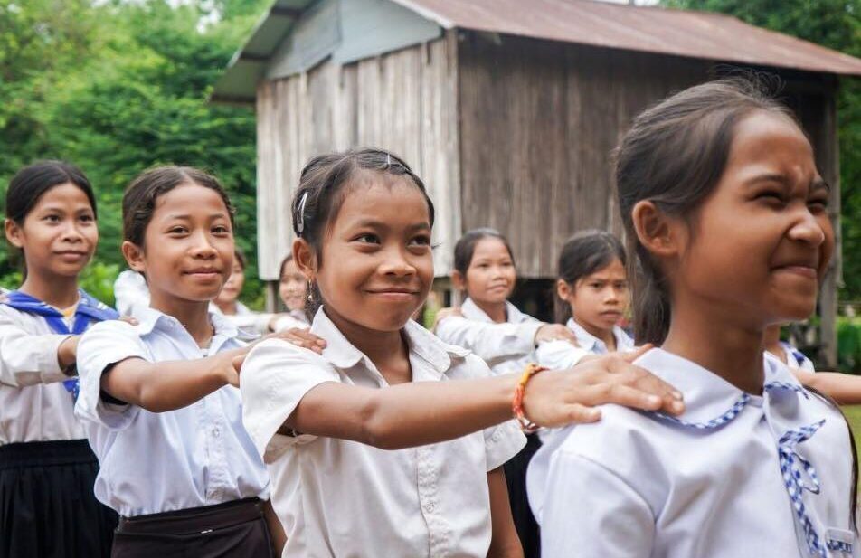Girls in school uniforms in a line smiling in a program with Plan International USA, a Carter partner