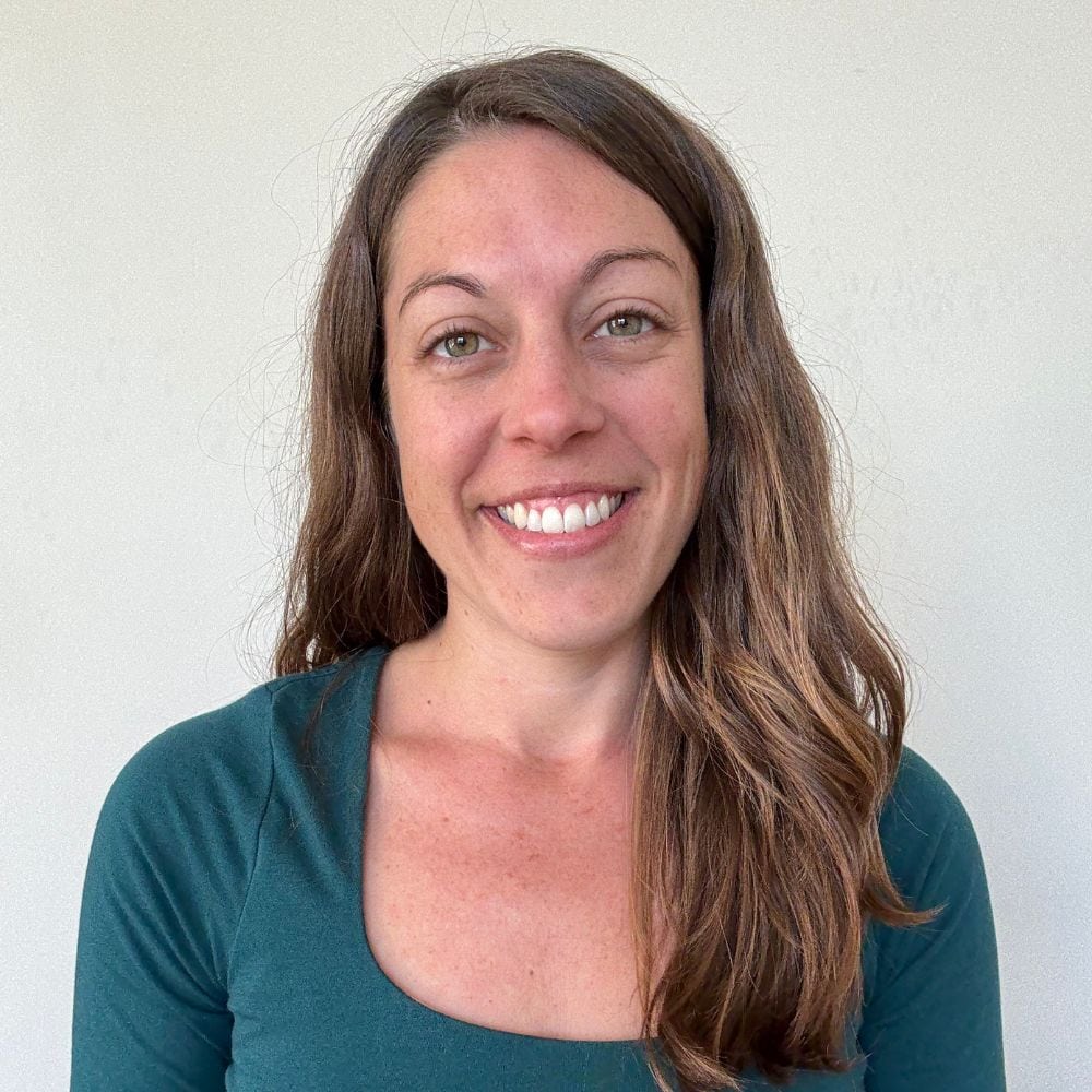 Smiling woman with long brown hair and green eyes in a teal top portrait.