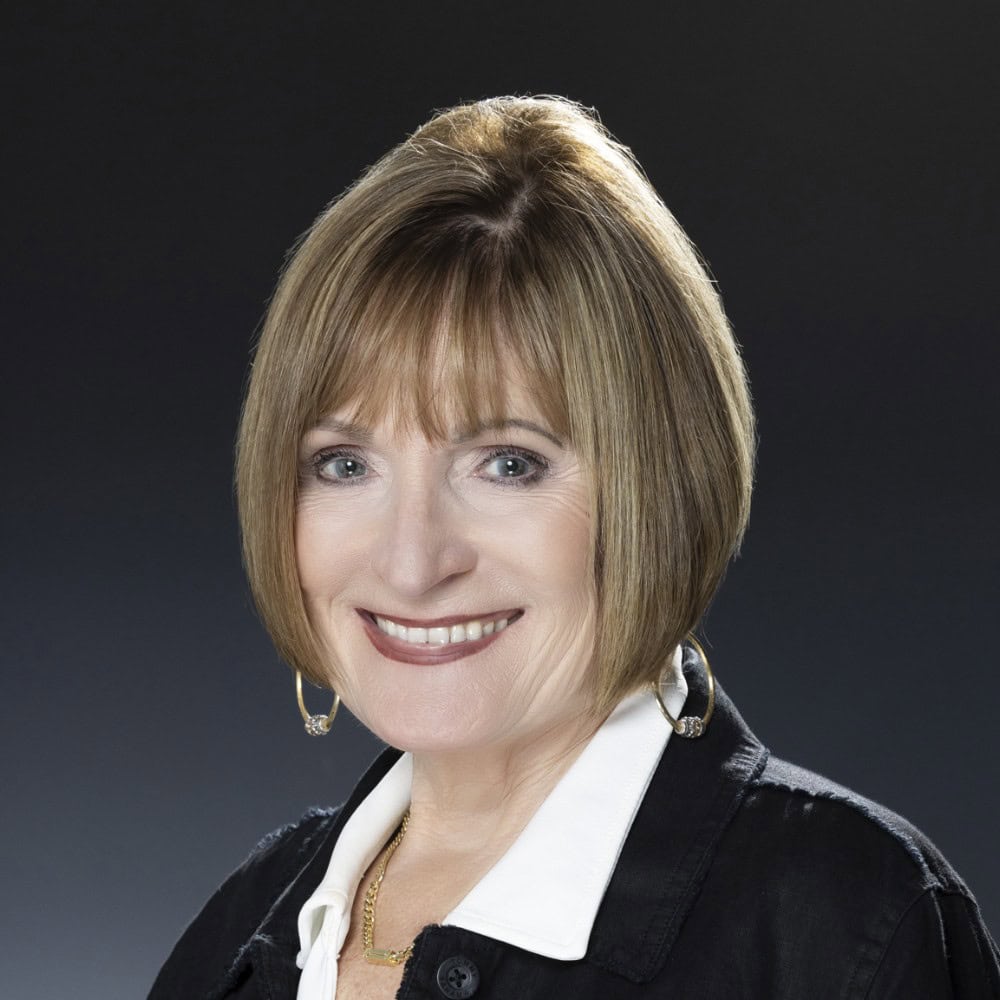 Warm friendly professional woman with short red hair, smiling, in black blazer and white shirt, portrait for business.