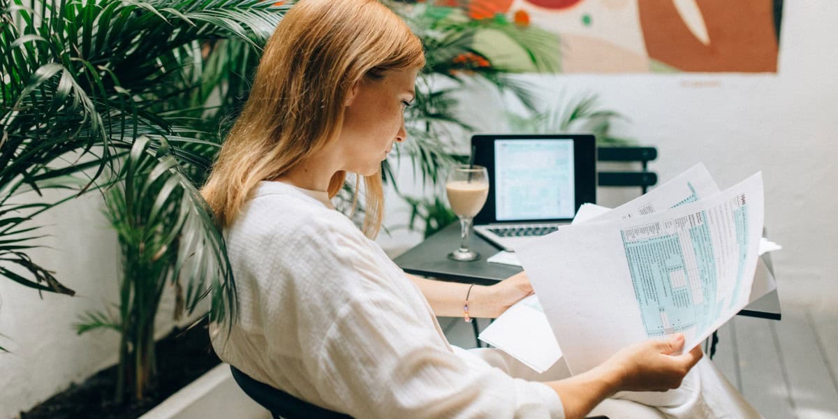 Financial professional reviewing documents in a modern office setting with a laptop and coffee.
