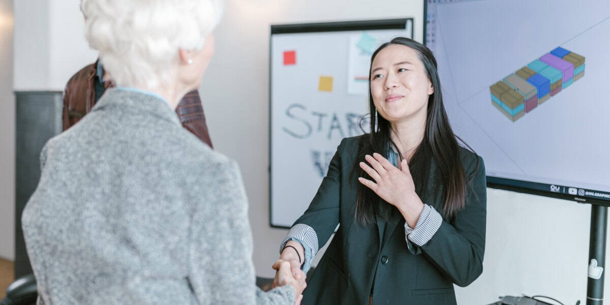 Businesswoman shaking hands with senior woman in office, professional greeting, career, networking, workplace, business environment, collaboration, success, CEO, professional relationship.