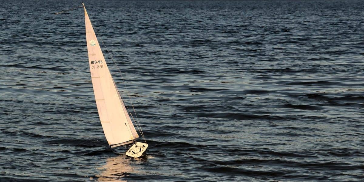A small model sailboat with white sails navigating through dark blue ocean waters, captured during a windy day, emphasizing marine recreation and sailing hobbies.