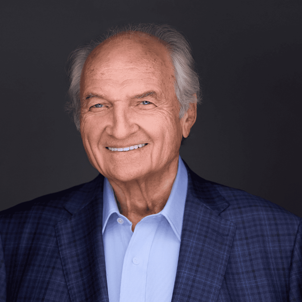 Smiling elderly man in a blue suit and light blue shirt.