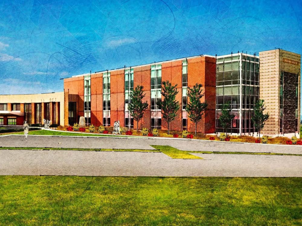 Modern academic building with brick and glass facade, surrounded by landscaped greenery and sculptures, showcasing healthcare architecture and campus environment for Bozeman Health, a Carter partner.