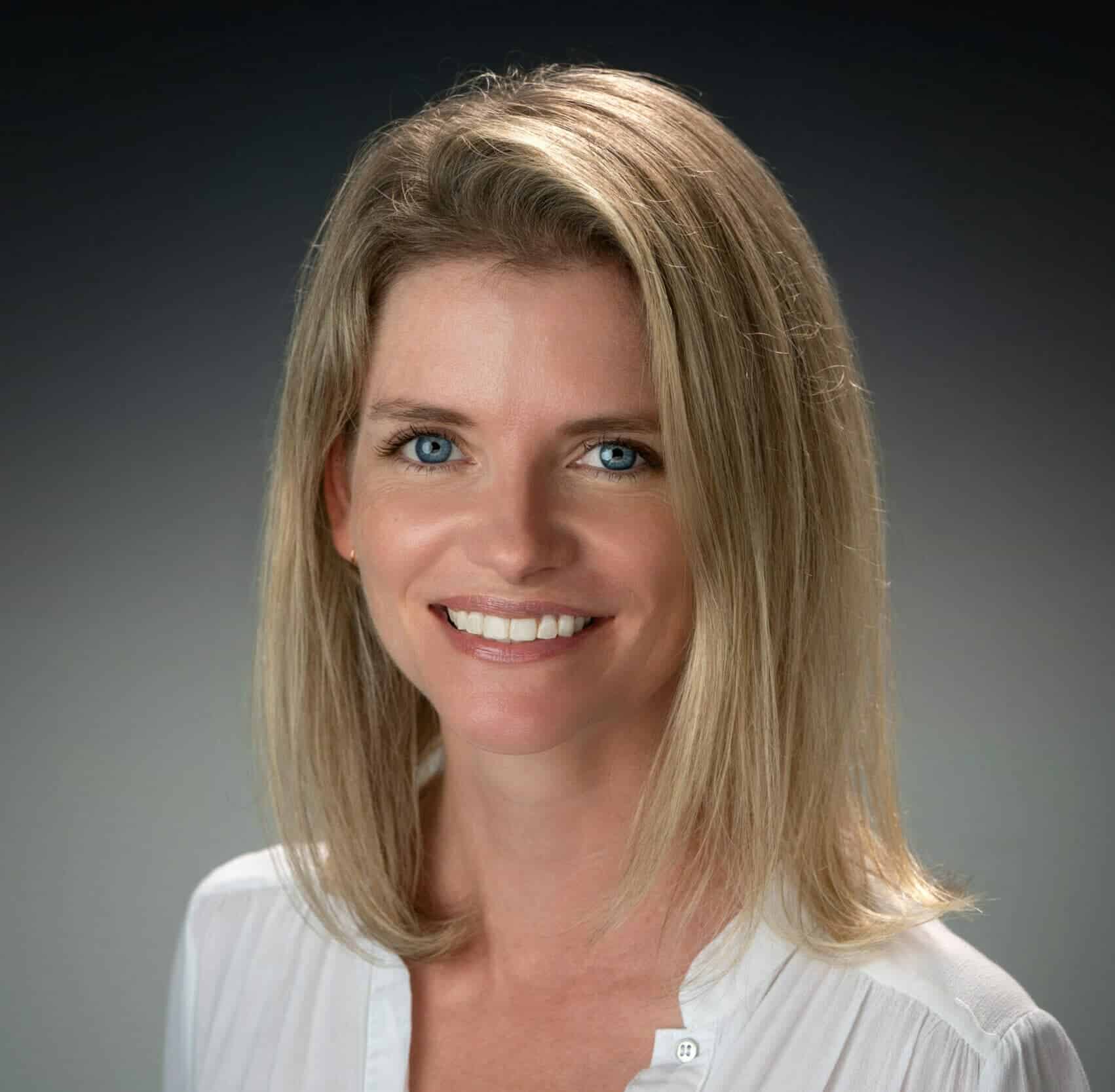 Bright smiling woman with blonde hair and blue eyes, professional headshot.
