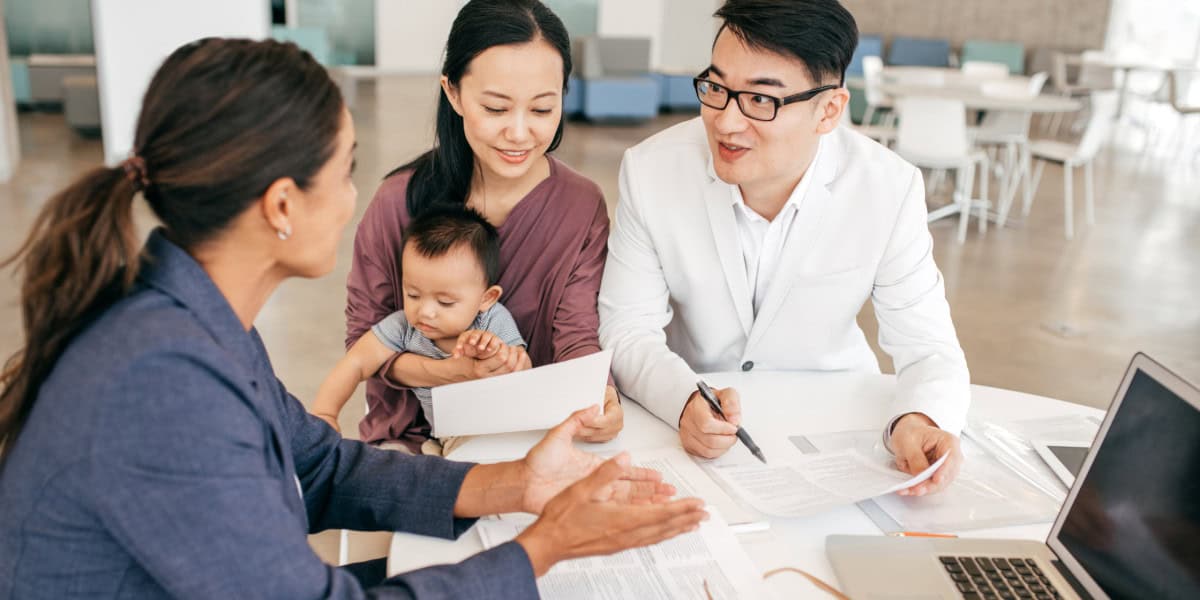 Multicultural family consulting financial advisor discussing documents at a modern office table.