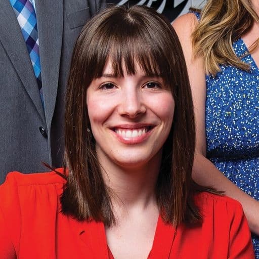 Bright smiling woman with shoulder-length brown hair and bangs, wearing a red blazer, showcasing professional fashion and confident demeanor.