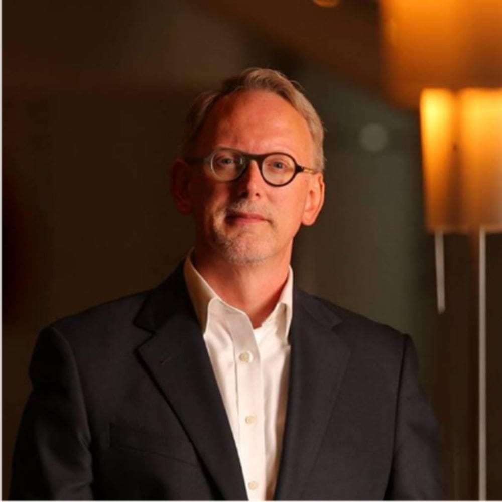 Elegantdressed middle-aged man in black suit and white shirt with glasses, posing in a professional setting, representing leadership and expertise.