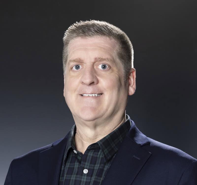 Senior businessman in formal suit with dark background, professional headshot for corporate profile.