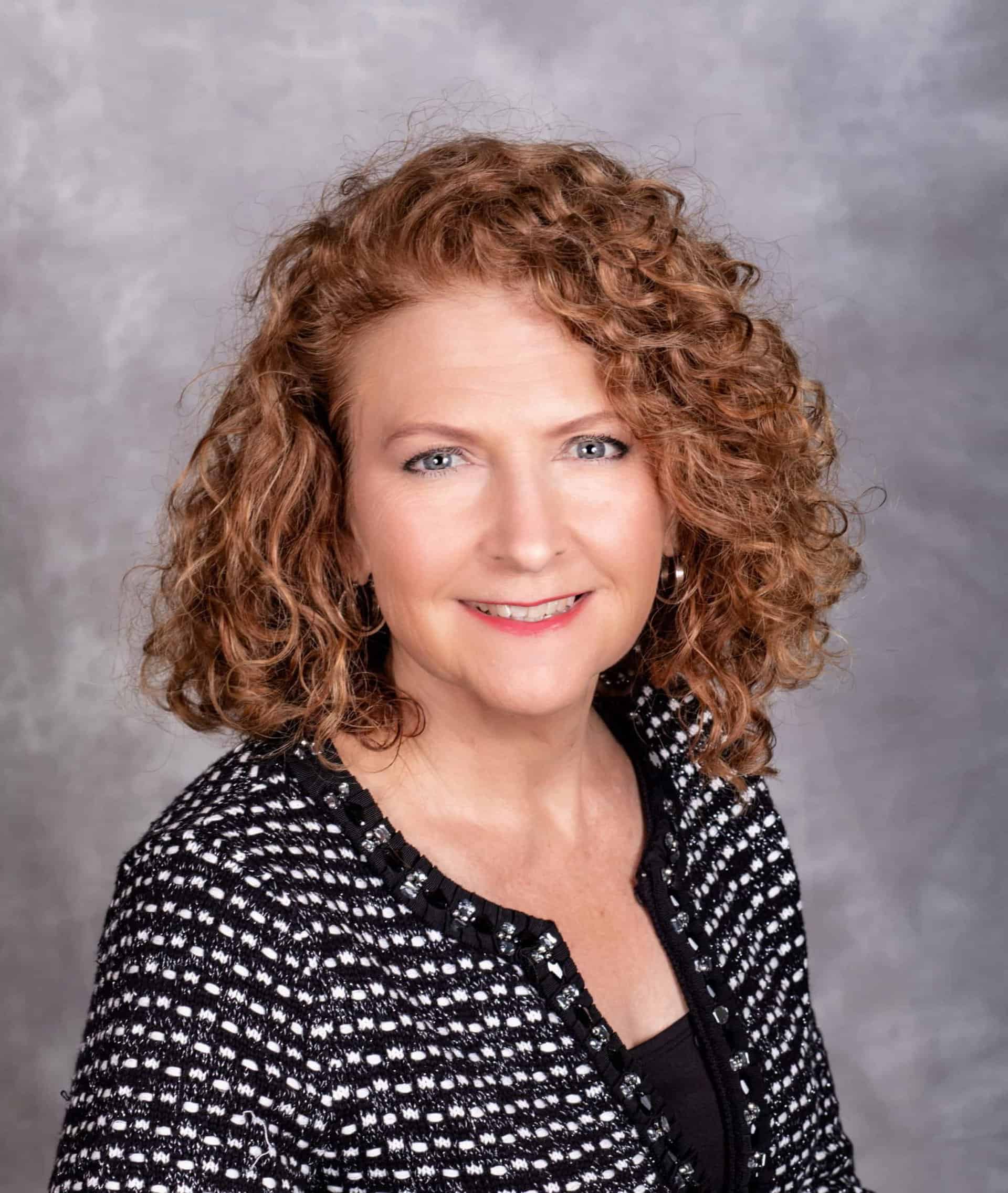 Beautiful professional headshot of a woman with curly red hair and blue eyes.