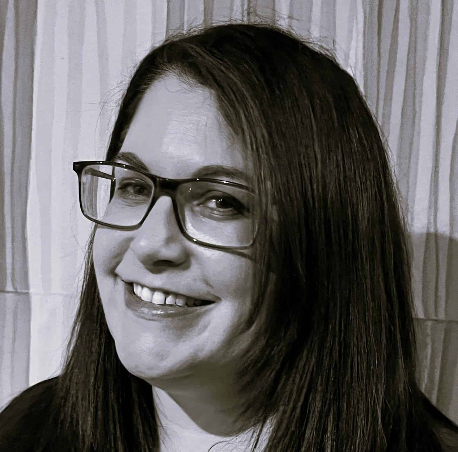 Portrait of a smiling woman with long dark hair, glasses, and a warm expression, emphasizing her cheerful personality and professional appearance.