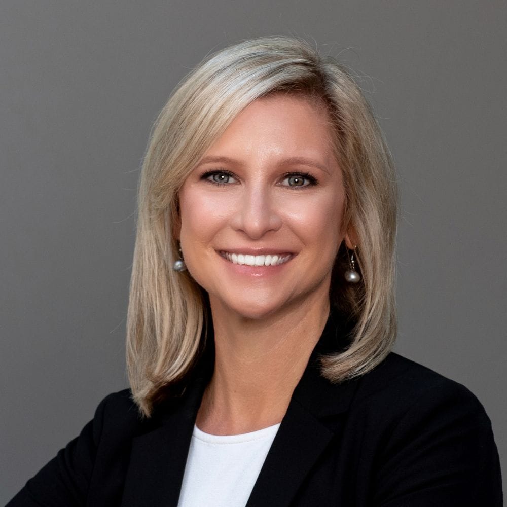 Professional woman in business attire with blonde hair, smiling confidently, representing leadership and success in corporate environments.