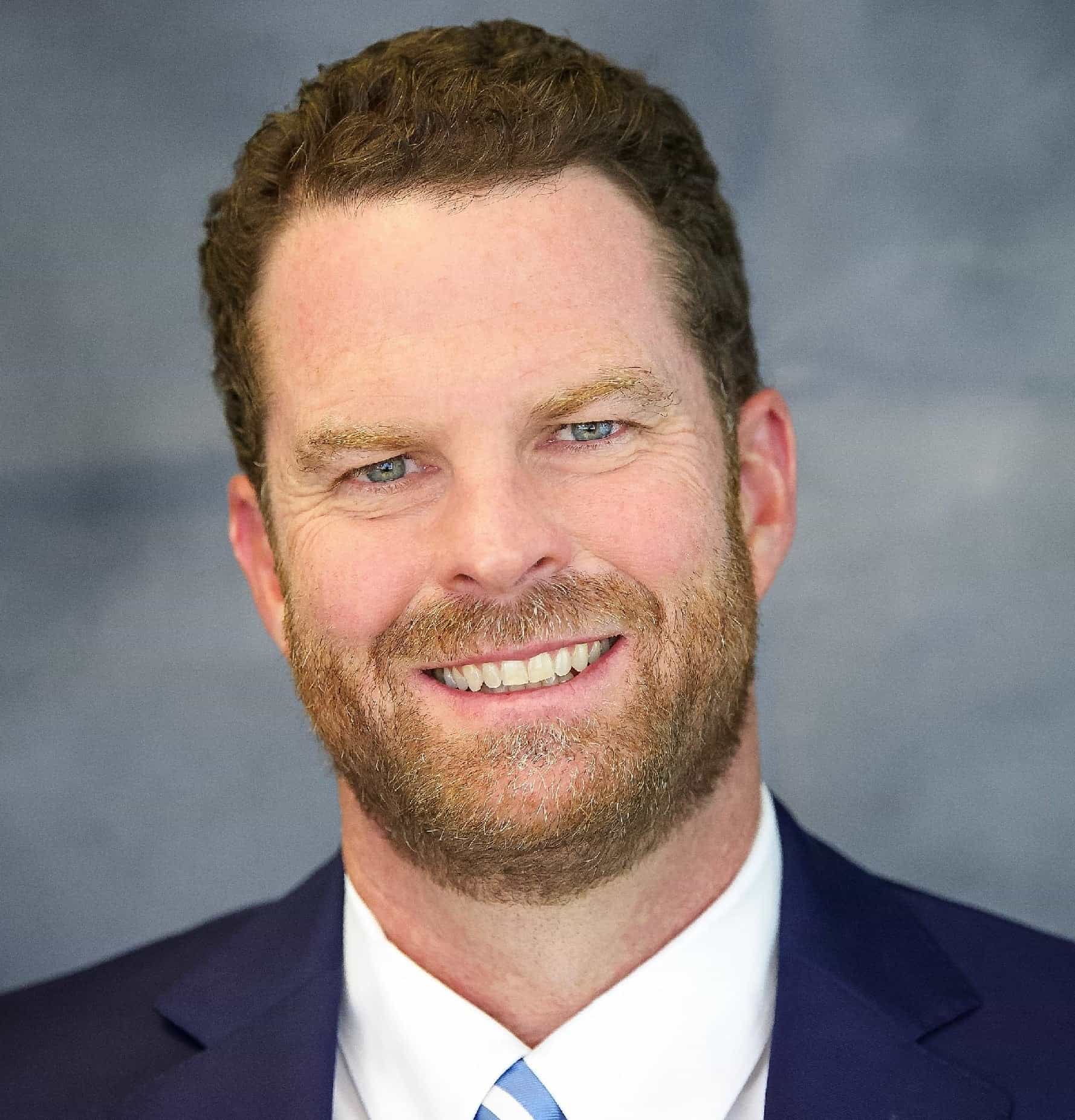 Close-up portrait of a smiling man wearing a navy suit and white shirt, professional headshot for business.