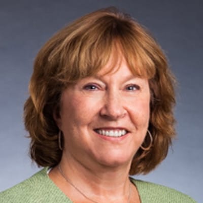 Professional woman with red hair and a green sweater smiling against a gray background.