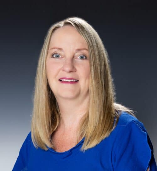 Confident woman with blonde hair wearing a blue top against a dark gradient background.