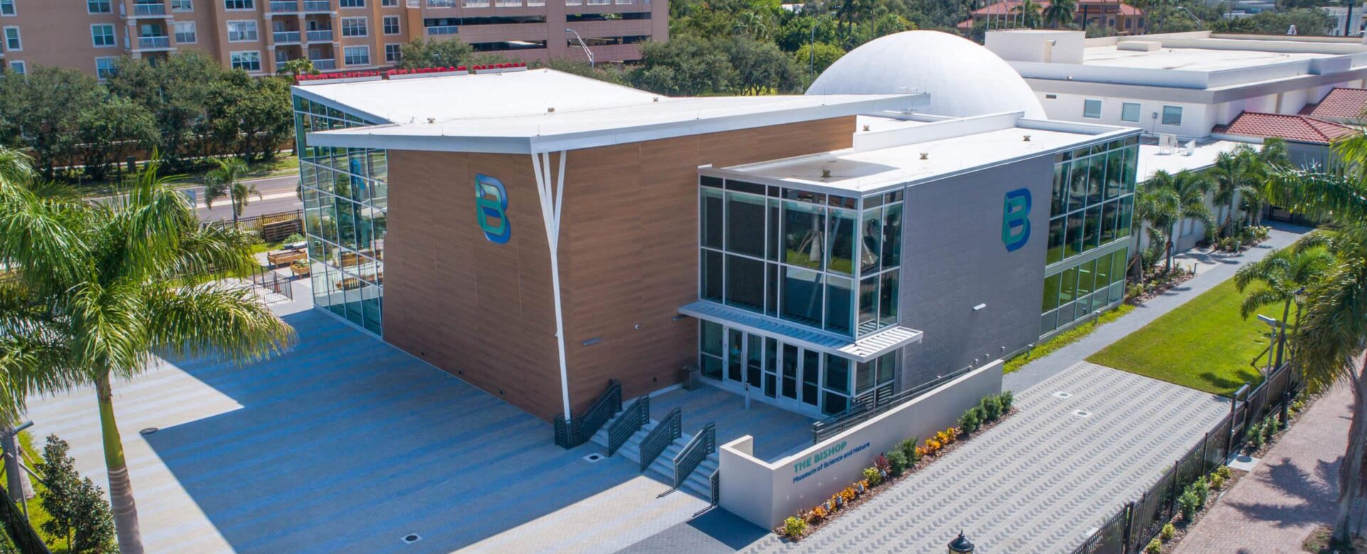 Photo of the new Bishop Museum of Science & Nature, a Carter partner. Modern multi-purpose community center with glass facade, outdoor green space, and surrounding residential buildings, featuring contemporary architecture and urban landscape design.