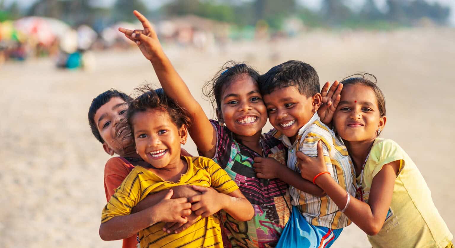 Vibrant group of smiling children playing together on a sandy beach in India, showcasing joy, friendship, and community.