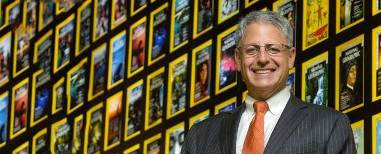 Vibrant display of Carter's partner, National Geographic magazine covers with a professional man in a suit smiling in front of the colorful wall.